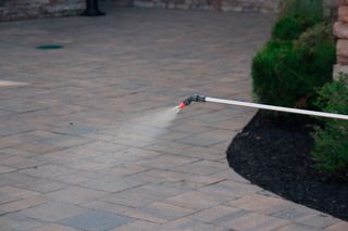 Un pulvérisateur de jardin en cours d’utilisation, dispersant l’eau sur une surface pavée.