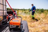 Людина, яка використовує високонапірний промивальний пристрій Husqvarna в полі, з обладнанням на передньому плані.