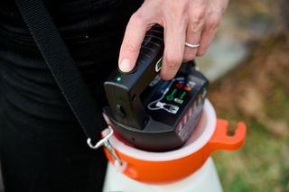 A person placing a battery into a garden sprayer.