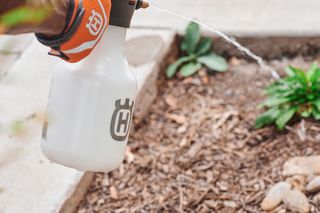 A person watering plants with a Husqvarna spray bottle in a garden.