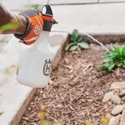 Une personne arrosant des plantes avec un vaporisateur Husqvarna dans un jardin.