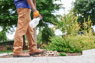 Une personne qui utilise un pulvérisateur de jardin pour appliquer un liquide sur les plantes d’un espace paysager.