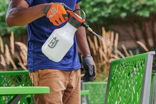 A person using a spray bottle to clean outdoor furniture in a garden setting.