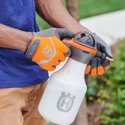 Une personne tenant un vaporisateur Husqvarna, portant des gants dans un jardin.