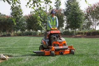 A person mowing lawn with a ride-on mower in a garden.