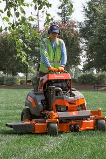 A person mowing lawn with a ride-on mower in a garden.
