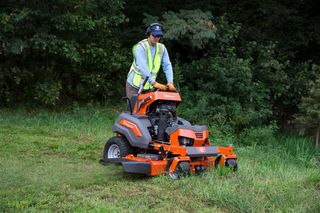 A person operating a ride-on mower on a grassy area with trees in the background.