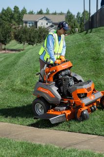 A person operating a ride-on lawn mower on a grassy slope in a residential area.