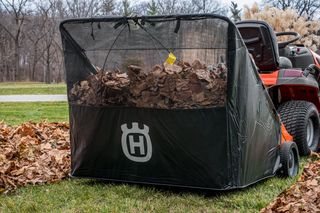 42" Lawn Sweeper. A leaf collector attached to a ride-on mower, filled with collected leaves in a garden.