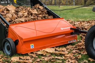 На трав'янистій ділянці трав'яниста ділянка містить сміттєзбірник Husqvarna, наповнений опалим листям.