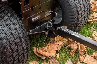 42" Lawn Sweeper. Close-up of a ride-on mower's locking differential and hitch on grass with fallen leaves.