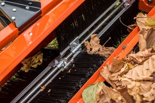 42" Lawn Sweeper. Close-up of a brush attachment on a machine with fallen leaves around it.