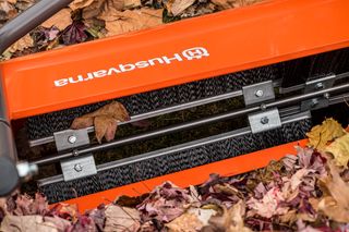 Close-up of a Husqvarna leaf sweeper with brushes, surrounded by fallen leaves.
