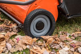 Close-up of a lawn mower wheel on grass with fallen autumn leaves.