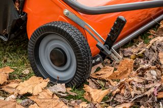 Close-up of a lawn mower wheel on fallen leaves and grass.
