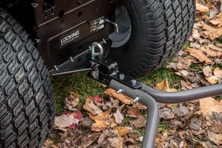 Close-up of a locking differential hitch on a lawn tractor amidst fallen leaves.
