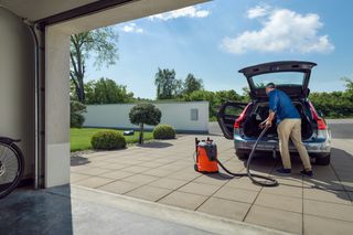 En person som använder en dammsugare för att rengöra bagageutrymmet på en bil som står parkerad på en uppfart.