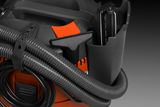 Close-up of a construction vacuum cleaner with hose attachments and storage compartment.
