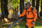 En person som använder en lövblåsare för att rensa bort nedfallna löv i en parkmiljö.