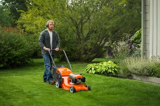 Husqvarna LC 140SP. Eine Person, die mit einem handgeführten Husqvarna-Rasenmäher einen Rasen mäht.