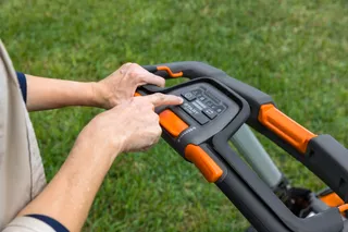 Uma pessoa a ajustar as definições num painel de controlo do cortador de relva num jardim.