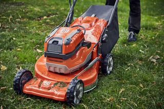 En person som använder en Husqvarna-gräsklippare på en gräsyta.