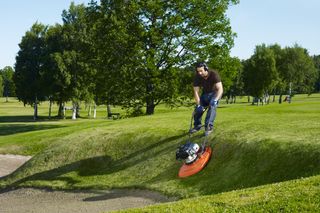 Une personne utilise une tondeuse sur coussin d’air pour couper l’herbe sur une pente dans un parc.