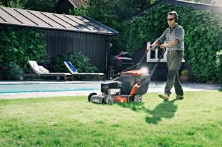 En person som klipper en gräsmatta bredvid en pool med en gräsklippare.