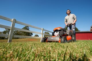 A person operating a ride-on lawn mower in a grassy area near a wooden fence.