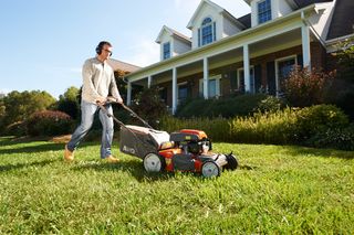 A person mowing lawn with a push mower in front of a large house.