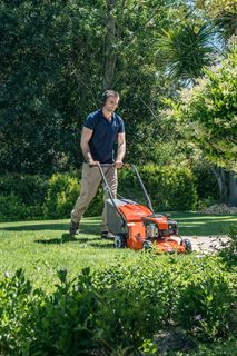 Una persona che taglia un prato con un tagliaerba a spinta in un giardino.