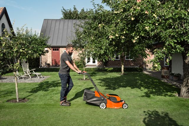 A person mowing a lawn with a push mower in a garden setting.