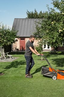 A person mowing a lawn with a push mower in a garden setting.