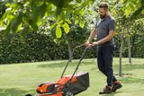 Ένα άτομο που κόβει ένα γκαζόν με ένα χλοοκοπτικό ώθησης σε ένα περιβάλλον κήπου.