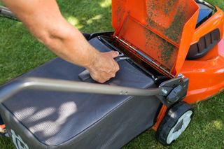 A person emptying the grass catcher of a lawn mower on a grassy area.