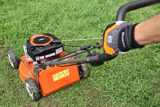 A person using a lawn mower on a grassy area, showcasing the control handle.