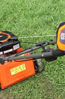 A person using a lawn mower on a grassy area, showcasing the control handle.