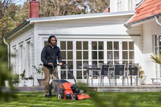 A person mowing lawn with a ride-on mower in a garden.