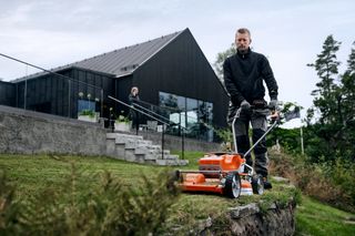 En person som klipper en gräsmatta med en handgräsklippare nära ett modernt hus.