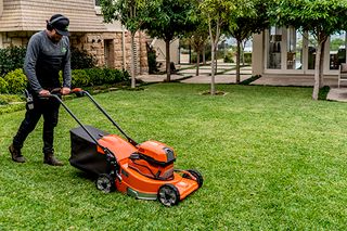 A person mowing a lawn with a push mower in a residential garden.