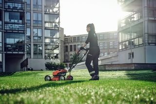 En person, der slår græs med en skubber plæneklipperen i en byhave.