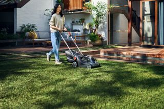 A person mowing lawn with a battery-powered lawn mower in a garden setting.