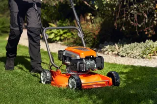 Tagliaerba Husqvarna LB 246E. Una persona che taglia il prato con un tagliaerba a spinta in un giardino.