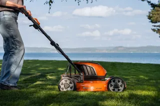 Eine Person, die mit einem Husqvarna Rasenmäher in der Nähe eines Sees einen Rasen mäht.