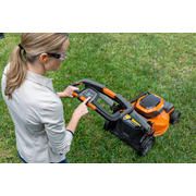 Une personne qui utilise une tondeuse à gazon, ajustant les réglages sur le panneau de commande dans un jardin.