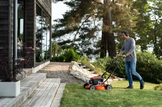 Husqvarna LB 244E. Eine Person, die in der Nähe eines modernen Hauses einen Rasen mit einem handgeschobenen Rasenmäher mäht.