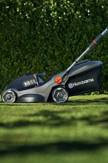 O persoană care tunde un gazon cu o mașină de tuns iarba Husqvarna.