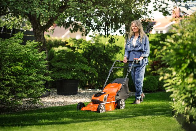 A person mowing a lawn with a push mower in a garden setting.