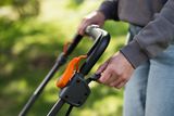 Eine Person, die den Griff eines Rasenmähers in einer Gartenumgebung einstellt.