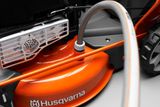 Close-up of a Husqvarna lawn mower deck with a hose connected, showcasing the mower's design.